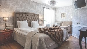 Dubbelrum med gråa tapeter, beige sängavel och kristallkrona