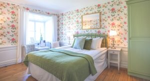 Dubbelrum med rosablommiga tapeter och säng med grönt överkast och kuddar