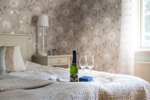 En flaska champange och två glas står på bricka på en säng i hotellrummet.