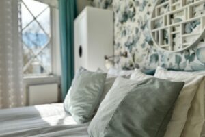 hotellrum med fokus på kuddar som är vita och turkosa, samt vitt väggskåp och tapeter med grönbladiga mönster.