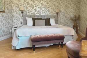 hotellrum med gammelrosa sittpall framför dubbelsäng. Ljusrosa överkast, naturfärgad sängavel och två sänglampor på vägen. Trägolv.