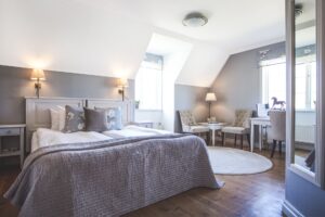 Hotellrum med dubbelsäng, vitt snedtak, vit matta och två beiga fotöljer.