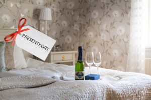 Rånäs champagneflaska samt 2 champagneglas på bricka som står på hotellsäng med vitt överkast.