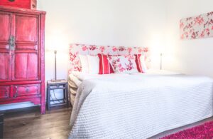 hotellrum med rött skåp, svart sängbord, rödblommig sänggavel och röda kuddar.